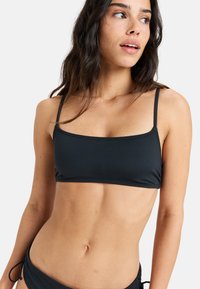 Čierny bikiny top so štvormiery otvorom a tenkými ramienkami, vyrobený z hladkej látky. Má minimalistický dizajn a priliehavý strih.