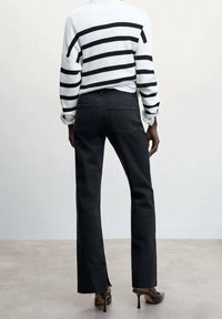 Pantalones de mezclilla negros acampanados con un dobladillo sin acabar, combinados con un suéter blanco ajustado con rayas horizontales negras.