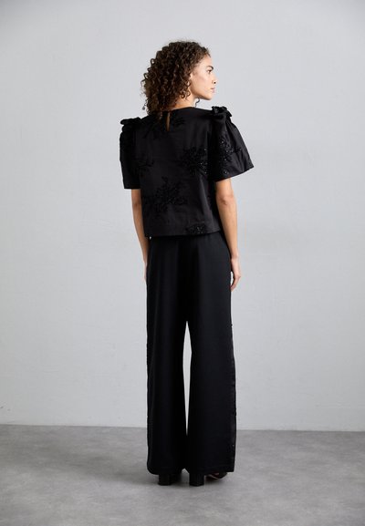 Top nero corto con maniche a sbuffo e dettagli in paillettes, abbinato a pantaloni neri a gamba larga, caratterizzati da una texture liscia e un design fluido.