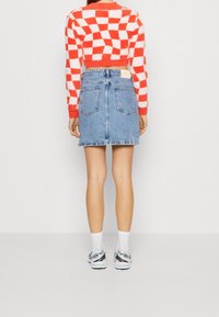 Pull court rouge et blanc à carreaux avec manches longues, associé à une jupe en denim bleu avec deux poches arrière et un ourlet légèrement effiloché.