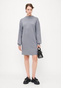 Grå strikket kjole med høy krage og oversized ermer, med rett snitt. Brukt med svarte klumpete sko og en liten veske.