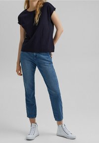 Marineblå tekstureret kortærmet top kombineret med lyseblå denim crop jeans og hvide højtop sneakers, der skaber et afslappet outfit.