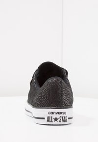 Czarny tenisówka z płótna o fakturowanej powierzchni, z białą gumową podeszwą i logo "Converse All Star" na pięcie. Widok od tyłu.