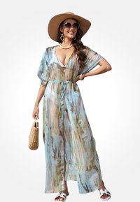 Kimono bleu clair transparent avec une ceinture nouée à la taille et des motifs abstraits multicolores. Manches larges et coupe décontractée, associé à un sac tressé.