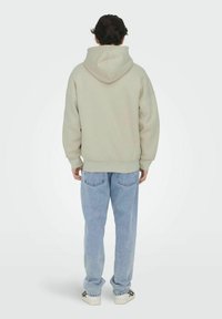 Lichtgrijze hoodie met een grote capuchon, ribgebreide manchetten en onderkant; gecombineerd met losse lichtblauwe jeans en witte sneakers.