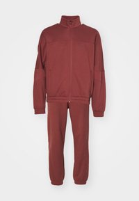 Bordo zip-up trenirka od mekog materijala. Ima visoki ovratnik, elastične manžete i pojas. Uključuje bočne džepove i uski kroj.