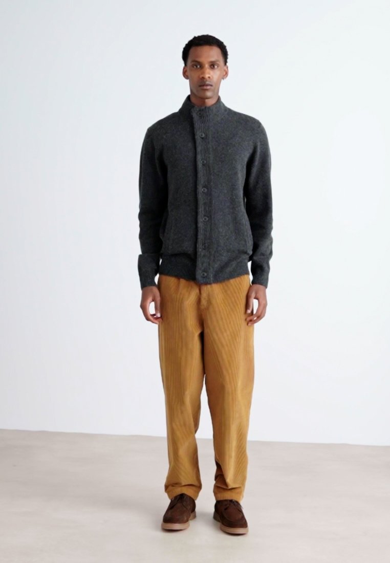 Cardigan gris foncé avec un col montant et une fermeture à boutons, associé à un pantalon en velours côtelé marron clair. Des chaussures marron complètent la tenue.