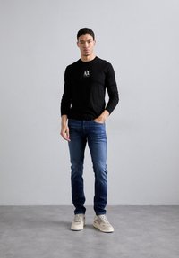 Black long-sleeve shirt with white logo, blue jeans, and beige sneakers. Casual fit, smooth fabric, medium texture, and simple design.