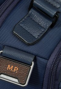 Tessuto blu navy strutturato con dettagli in pelle, caratterizzato da una targhetta rettangolare in metallo con le iniziali "M.P." e il nome del marchio "Piquadro".