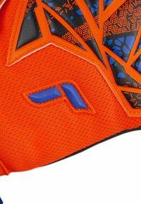 Parte superiore di scarpa sportiva di un vivace arancione, caratterizzata da un materiale a rete testurizzato, accenti neri e motivi geometrici blu con dettagli del logo modellati.