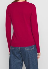 Fuchsia tröja med långa ärmar och rund halsringning, tillverkad av mjukt stickat tyg; kombinerad med löst sittande blå denim-byxor.