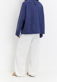 Navy blue, lightweight cotton jacket with a relaxed fit and shoulder seam details. Paired with white pants featuring vertical blue stripes.