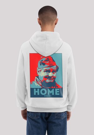 White hoodie featuring a graphic print on the back of a man in a cap, with the text "HOME GUARD" below, set against red and blue backgrounds.