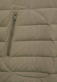 Section de veste rembourrée verte olive avec une poche zippée au design horizontal et un motif cousu pour l'isolation.
