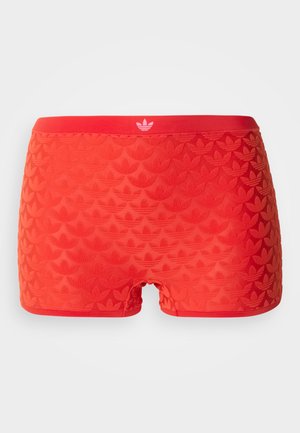 Φανταχτερά κόκκινα ελαστικά σορτς με ανάγλυφα λογότυπα Adidas trefoil σε όλη την επιφάνεια και μια μονόχρωμη κόκκινη ζώνη μέσης με λευκό λογότυπο trefoil στο κέντρο μπροστά.