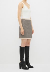 Top en jersey blanc ajusté avec un décolleté en V, associé à une mini jupe en tweed marron avec un motif texturé et un ourlet crème. Bottes noires à talons hauts jusqu'aux genoux.