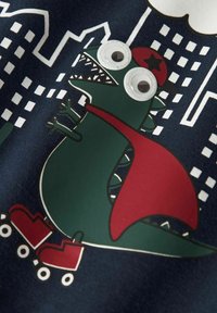 Gráfico de dinosaurio verde sobre tejido azul oscuro, con una capa roja y patines de ruedas. Presenta ojos saltones y un patrón de paisaje urbano en el fondo.