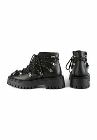 Botas de piel negra hasta el tobillo con suelas de goma gruesas, con cordones y herrajes metálicos. Parte superior texturizada con acentos de lazo en los lados.