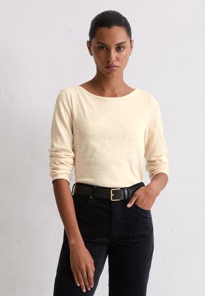 Lichtbeige langemouwen top met een wijde halslijn, gecombineerd met zwarte broek en een zwarte riem met een gouden gesp. Gladde textuur.