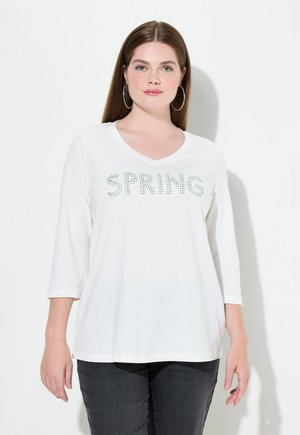Weißes V-Ausschnitt Langarm-T-Shirt mit dem Aufdruck "SPRING" in grünen Strasssteinen. Weicher Stoff mit einer lockeren Passform, kombiniert mit dunklen grauen Hosen.