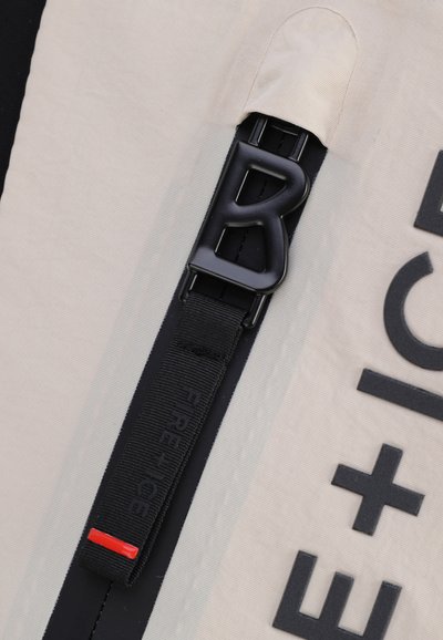 Bela tkanina z teksturiranim zaključkom ima črn plastičen zaponko in trak z oznako "FIRE + ICE," okrašena z rdečo črto.