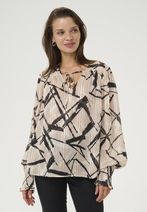 Loose-fitting beige blouse with a black abstract pattern, featuring a V-neck with tie detail and elasticized cuffs. Smooth fabric with subtle shine.