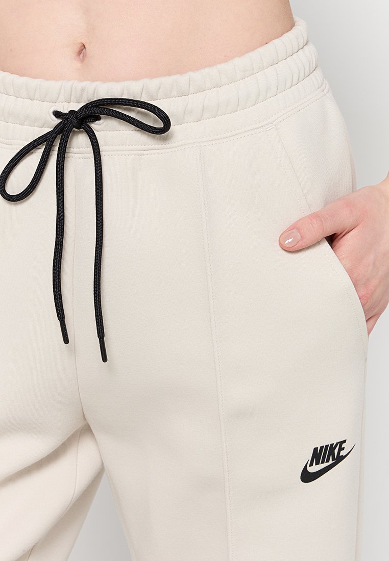 Pantalones de chándal beige de Nike con cordón negro, bolsillo lateral y logo bordado; confeccionados con una tela suave, elástica y cómoda.