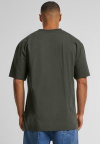 Dark green oversized t-shirt with short sleeves and a crew neck. Smooth texture, simple design, with a straight cut at the hem.