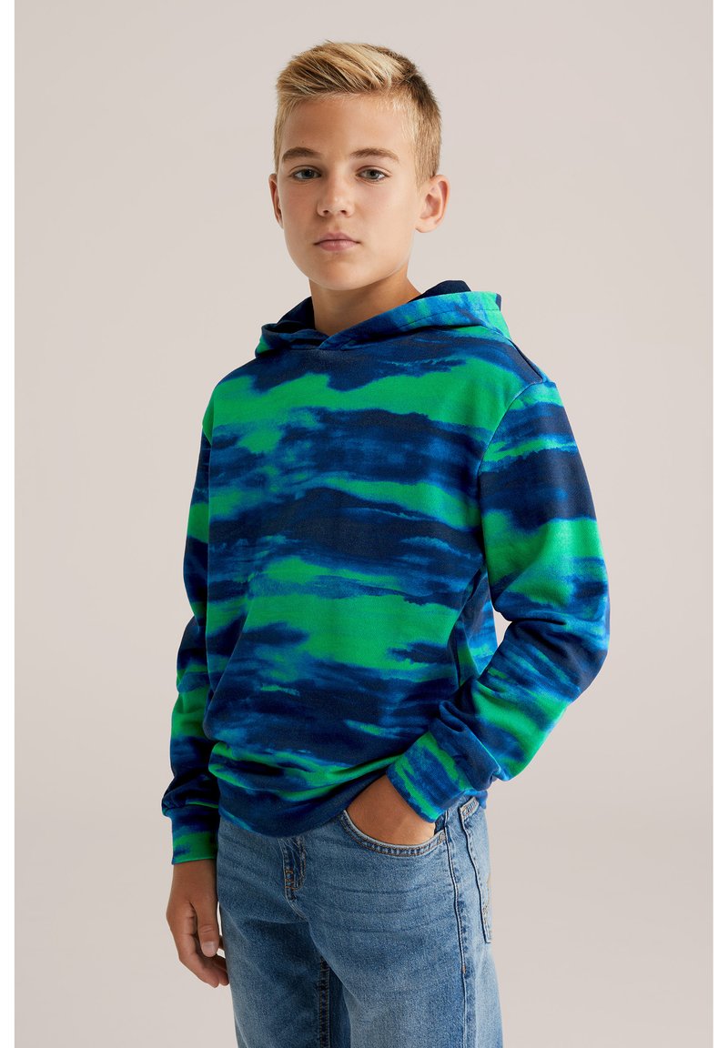 Felpa con cappuccio in un motivo tie-dye blu e verde, realizzata in tessuto morbido. Presenta maniche lunghe e una tasca frontale, indossata con jeans di denim.