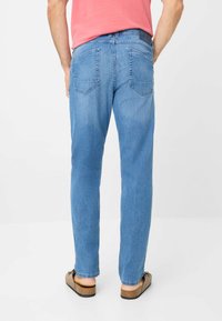 Jeans in denim blu chiaro con vestibilità dritta, dotati di due tasche posteriori e cuciture sottili. Indossati con sandali marroni senza chiusura.