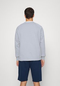 Sudadera gris claro con mangas largas y cuello redondo, que presenta puños acanalados. Combinada con pantalones cortos azul marino, de textura mezcla de algodón, diseño casual.