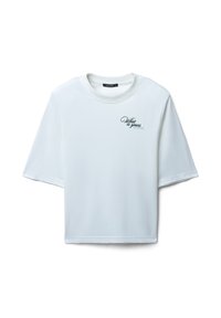 T-shirt blanc à manches courtes en coton avec une coupe décontractée. Il présente un petit design de texte scripté noir sur la zone gauche de la poitrine.