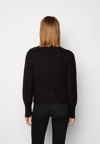 Maglione nero lavorato a maglia con texture a coste, maniche lunghe e vestibilità corta, visto da dietro su uno sfondo neutro.