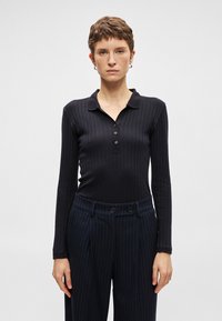 Camisa polo preta de manga longa com textura canelada e pala de três botões, combinada com calças azul-marinho com riscas e botões duplos.