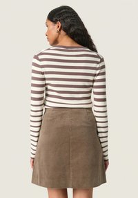 Ribbet langærmet top i beige og brun, parret med en brun fløjl A-linje nederdel. Stoffet ser blødt ud med en subtil ribbet tekstur.