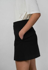 Sort nederdel med en tætsiddende talje, sidelommer og lige snit. Stoffet fremstår glat med minimale syninger, kombineret med en hvid top.