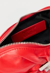 Κόκκινη δερμάτινη τσάντα χειρός με υφή, κλείσιμο με φερμουάρ και μαύρο εσωτερικό. Διαθέτει κόκκινη ετικέτα με λογότυπο και διακοσμητικό ασημένιο στοιχείο.