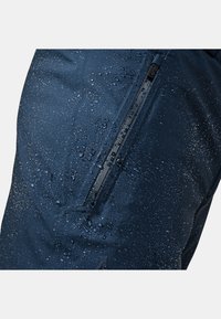 Navy wasserdichte Hose mit einem Reißverschlusstaschen, sichtbar Wassertröpfchen auf einer glatten Stoffoberfläche und in matter Optik.