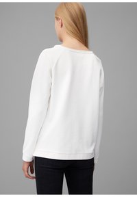 Felpa bianca con collo tondo, maniche raglan e polsini a coste, che mette in mostra una texture liscia e morbida. Indossata con jeans scuri.