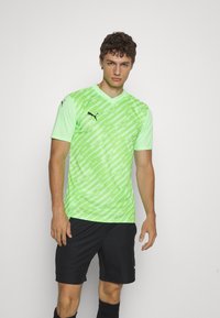 Gaiši zaļš sporta krekls ar ģeometrisku rakstu, V veida dekoltē, īsām piedurknēm un melnu Puma logo uz krūtīm un pleca.