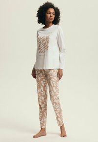 Biała piżama z długim rękawem zdobiona roślinnym wzorem w jasnobrązowym kolorze. Pasujące jasnobrązowe spodnie z białymi liśćmi. Materiał bawełniany.