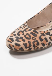 Gros plan sur une chaussure plate en imprimé léopard avec des taches beige, noir et orange sur un matériau en suède doux, contre un fond blanc.