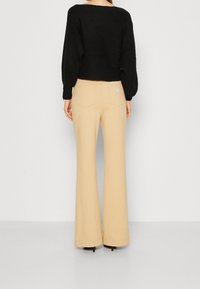 Pull court noir en tricot à manches longues, associé à un pantalon évasé beige taille haute avec un petit logo de la marque sur la poche arrière.