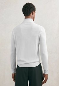 Pulover polo alb cu mâneci lungi, din material moale, cu guler și manșete ribbed, design mulat și aspect minimalista.