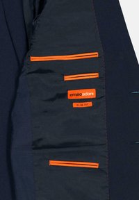 Innenansicht eines Marineblazers mit vier Taschen, die orangefarbene Reißverschlüsse und orangefarbene Nähte aufweisen. Enthält ein rotes Etikett mit der Aufschrift "emilio adani SLIM FIT."