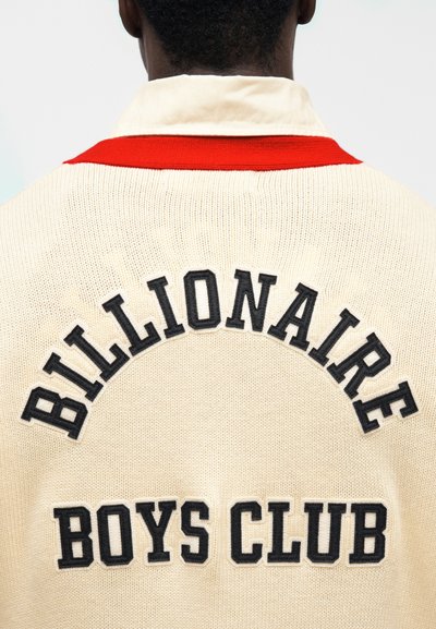 Ζακέτα πλεκτή κρεμ χρώματος με κόκκινο γιακά. Διαθέτει μαύρα κεντημένα γράμματα: «BILLIONAIRE BOYS CLUB» σε καμπυλωτό σχέδιο στην πλάτη.