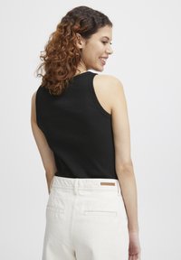 Débardeur noir à côtes avec un col rond, associé à un pantalon beige clair taille haute avec des poches arrière et un détail en cuir.