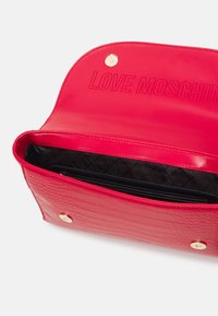 Borsa a mano effetto pelle rossa con texture coccodrillo, chiusura a scatto dorata e logo "LOVE MOSCHINO" impresso; interno nero a fantasia con tasca con zip.
