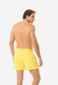 Gelbe Badehose mit elastischem Bund, aus leichtem Material hergestellt. Ausgestattet mit einer einfarbigen Gestaltung und einem schlichten Design ohne Muster.