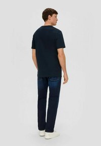 Dunkelblaues Baumwoll-T-Shirt mit klassischem Rundhalsausschnitt, kombiniert mit dunklen Denim-Jeans und weißen Sneakers für ein lässiges Outfit.